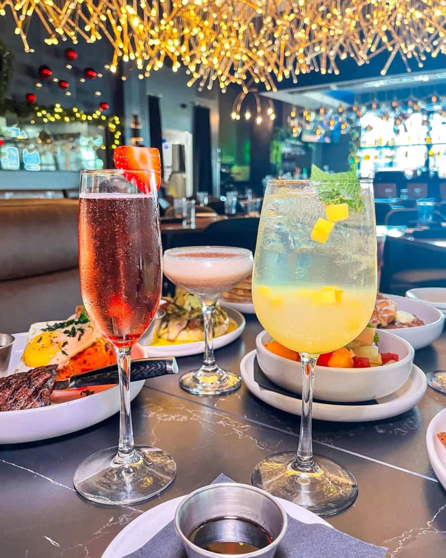 A sparkling blackberry mimosa and a mango cocktail on the bar beneath Tallo's gold twig chandelier